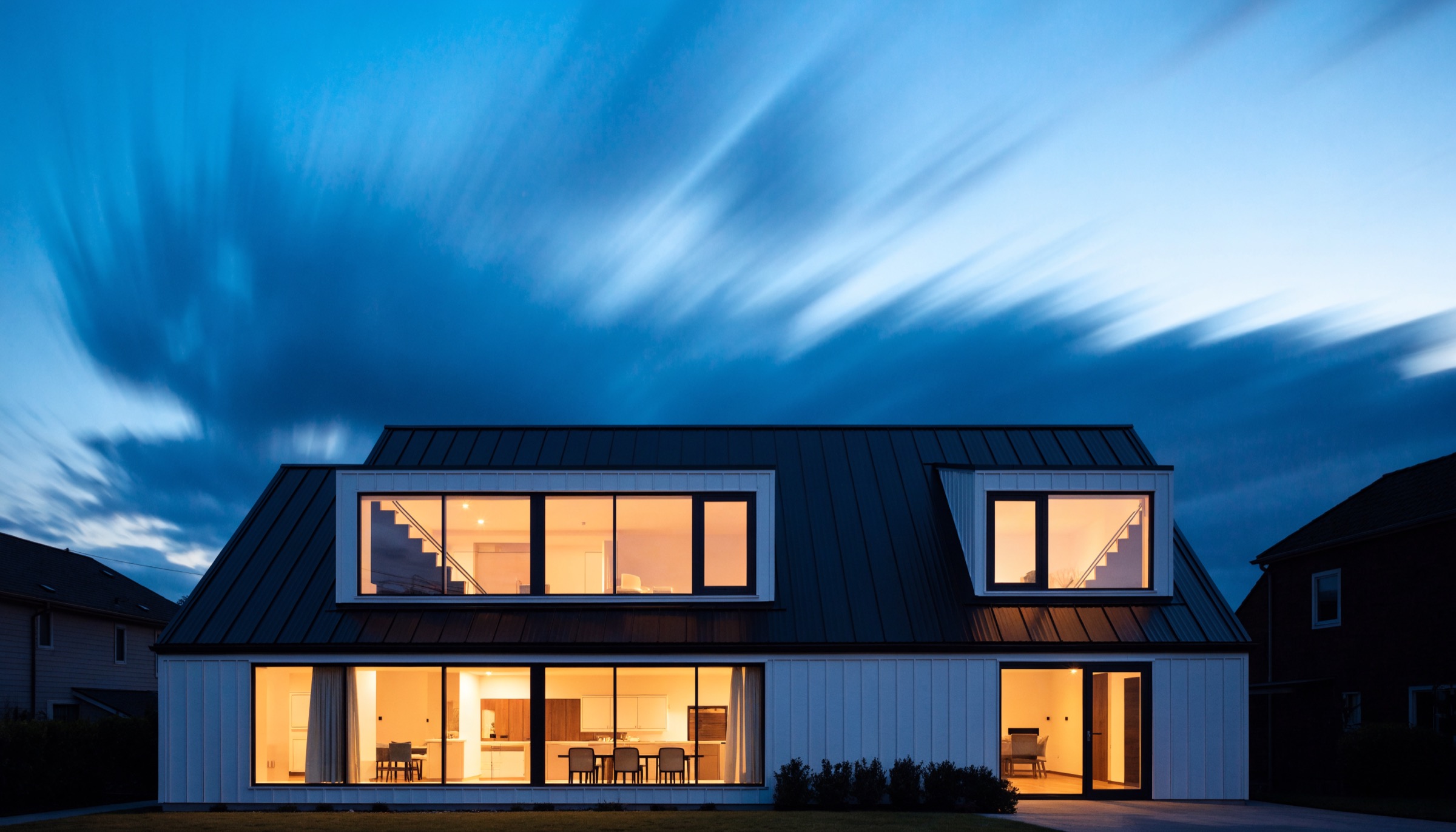 A contemporary home at dusk with warmly lit windows